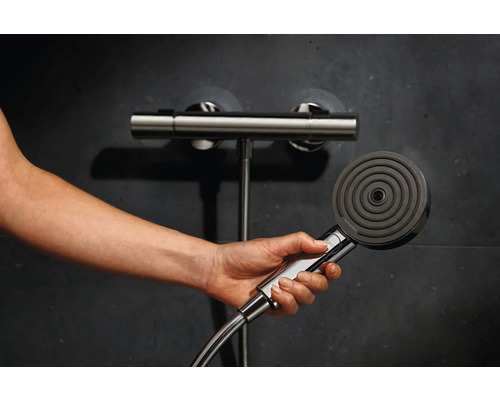 Hand hält eine Hansgrohe Handbrause vor einer Duscharmatur.