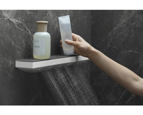 Badezimmer Szene mit Duschkopf, der Wasser sprüht, und einer Hand, die eine Kosmetik Tube hält, auf einem Regal stehen Duschgel und eine Lotion.