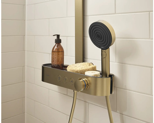 Système de douche avec étagère, douchette à main, savon et lotion sur fond de carreaux blancs.