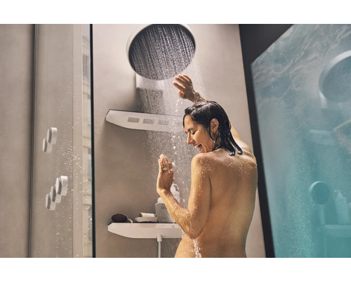 Frau duscht unter einer Kopfbrause in einem Badezimmer mit Ablageregalen.