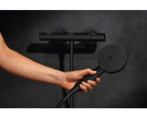 Une main tient une pomme de douche devant un mitigeur thermostatique