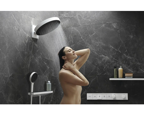 Frau unter einer Kopfbrause in einem Badezimmer mit Marmorwänden.