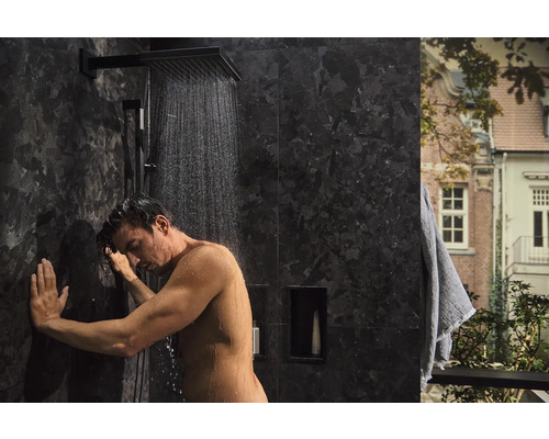 Badezimmer mit einer Person unter einer Regendusche mit dunklen Fliesen
