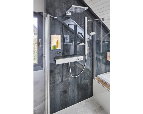 Cabine de douche avec douche de tête, douchette à main, thermostat et étagères de rangement dans une salle de bains avec des carreaux muraux foncés et un toit en pente.