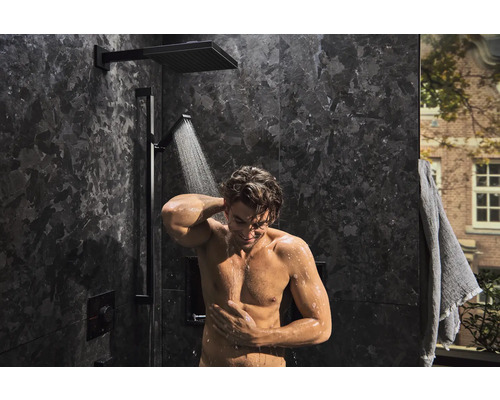 Mann unter einer Duscharmatur mit Kopf- und Handbrause in einem modernen Badezimmer