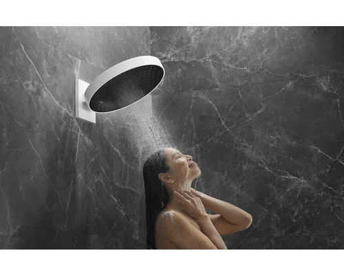 Frau unter einer runden Kopfbrause in einer Dusche mit Marmorwand.
