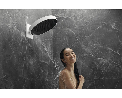 Frau unter einer runden Kopfbrause mit Wasserstrahlen in einem Badezimmer mit Marmorwand