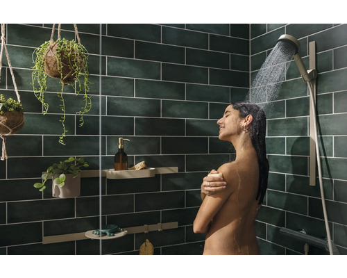 Frau unter der Dusche mit Duschkopf und grünen Wandfliesen sowie Deko-Elementen