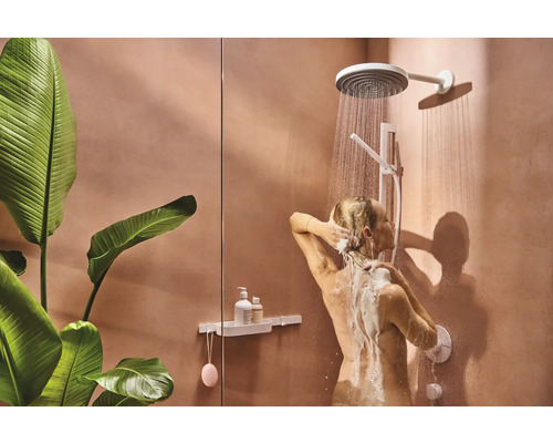 Frau unter der Dusche mit Kopfbrause und Handbrause in einem Badezimmer mit Pflanzen.