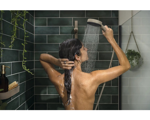 Frau unter der Dusche mit Handbrause in einem gefliesten Badezimmer