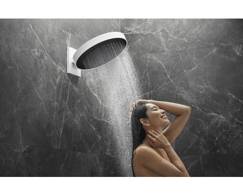 Frau unter einer runden Kopfbrause mit Wasserstrahl in einem Badezimmer mit Marmorwänden.