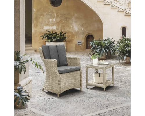 Ensemble de balcon Destiny Luna 2 pces naturel chiné, 1 fauteuil + table, rotin synthétique + aluminium, y compris galettes d'assise Scène de jardin avec fauteuil en rotin et table d''appoint en rotin avec plateau en verre sur une terrasse