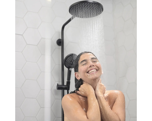 Frau unter einer Kopfbrause mit Handbrause im Badezimmer