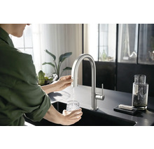 Frau füllt ein Glas Wasser an einem Küchenspültisch mit einem Wasserhahn
