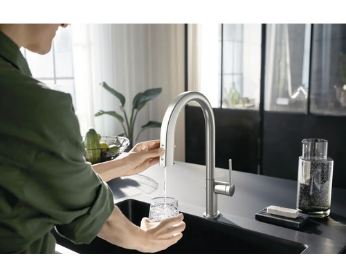 Frau füllt ein Glas Wasser an einem Küchenspültisch mit einem Wasserhahn