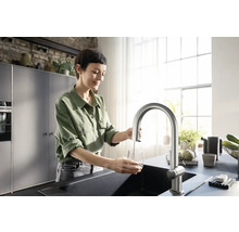 Frau befüllt ein Glas mit einem Wasserhahn in einer modernen Küche.
