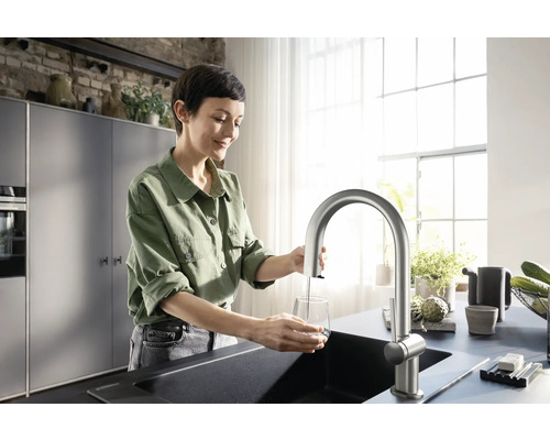 Frau befüllt ein Glas mit einem Wasserhahn in einer modernen Küche.