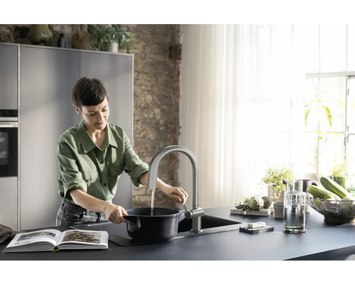 Frau am Waschbecken mit Spültischarmatur und Kochtopf in einer modernen Küche