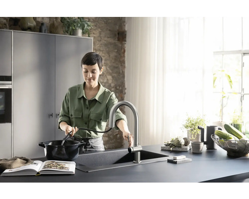 Frau befüllt einen Topf mit Wasser an einer Küchenspüle mit ausziehbarer Armatur in einer hellen Küche.