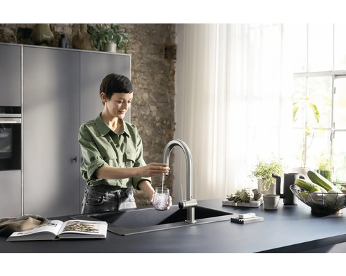 Frau füllt Wasser in ein Glas an einem Spültisch mit Armatur in einer hellen Küche.