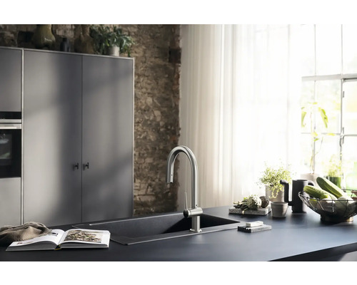 Küchenszene mit Spüle, Armatur, Kochbuch und Dekoration auf einer dunklen Arbeitsplatte vor einer Backsteinwand