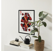 Gerahmtes Deadpool-Poster über einem Regal mit Büchern, einer Kamera, einer Gießkanne und einer Pflanze.