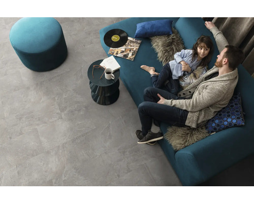 Salon avec carrelage de sol gris imitation pierre, canapé, tabouret et table basse