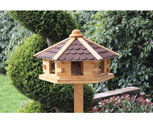 Nichoir avec toit et silo à nourriture sur un poteau en bois dans le jardin.