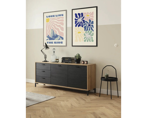 Wohnzimmer mit Kommode, Tischlampe, Dekorationsgegenständen und zwei gerahmten Postern an der Wand