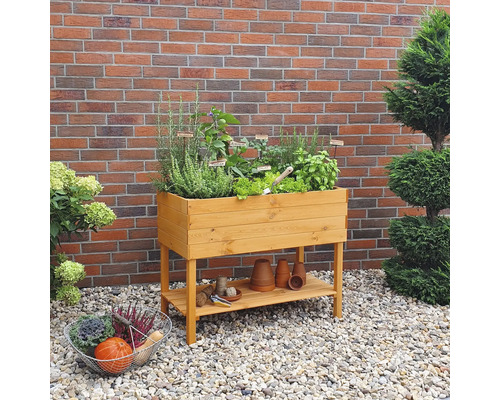 Jardinière surélevée en bois avec herbes et légumes dans le jardin devant un mur en briques
