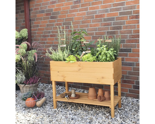 Jardinière sur pieds en bois avec herbes et légumes devant un mur de briques