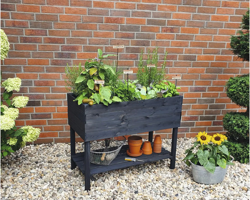 Jardinière surélevée en bois avec herbes et légumes sur une terrasse avec des pierres