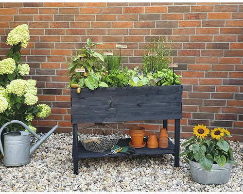 Jardinière en bois avec herbes, légumes, outils et plantes devant un mur de briques