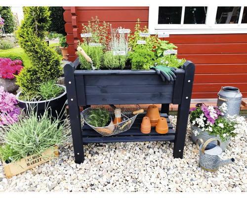 Jardinière surélevée en bois avec herbes aromatiques, outils de jardin et décoration devant un mur en bois rouge