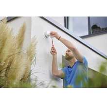 Ein Mann montiert eine Aussenleuchte mit einem Schraubenzieher an einer Hauswand.
