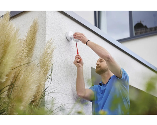 Ein Mann montiert eine Aussenleuchte mit einem Schraubenzieher an einer Hauswand.