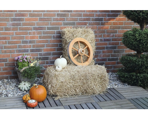 Dekoratives Herbstarrangement mit Heuballen, Kürbissen und einem Holzrad vor einer Backsteinmauer.