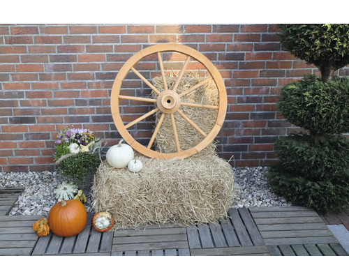 Roue de charrette grand modèle en bois Ø 90 cm h 22 cm couleur miel Scène décorative avec roue en bois, botte de paille et citrouilles devant un mur en briques.