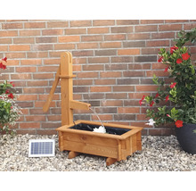Holzbrunnen mit Solarpanel vor einer Ziegelwand