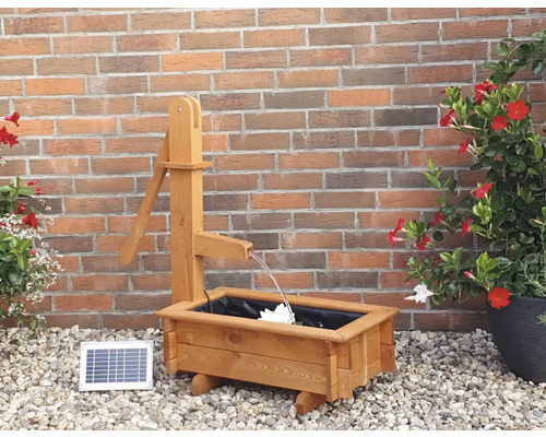 Holzbrunnen mit Solarpanel vor einer Ziegelwand
