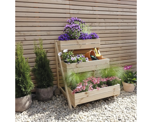 Dreistufiges Holzregal mit Blumen und Gartengeräten vor Holzwand