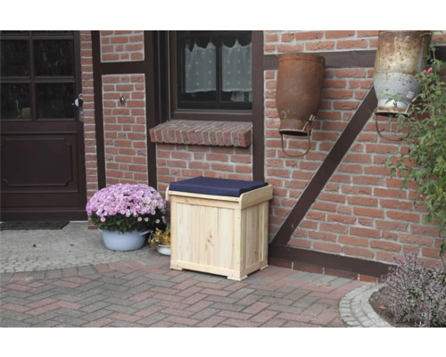 Malle à coussins Patrick 56 x 43 cm bois naturel y compris galette d'assise bleue Coffre en bois avec coussin d''assise bleu devant un mur de briques