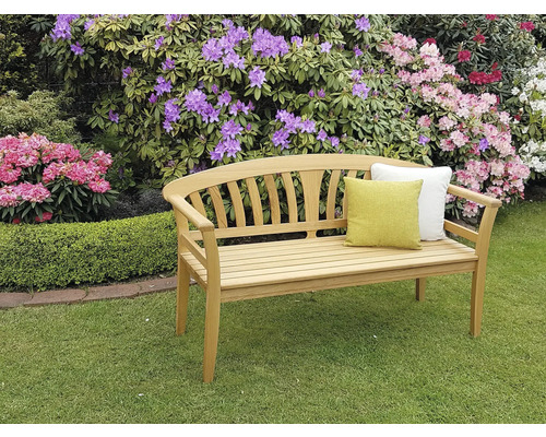 Holzgartenbank mit Kissen vor blühenden Büschen
