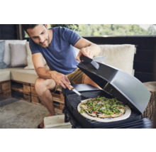 Un homme fait griller une pizza sur un gril d''extérieur