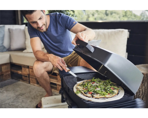 Un homme fait griller une pizza sur un gril d''extérieur