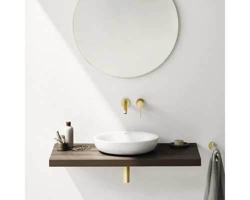 Salle de bains moderne avec miroir rond, vasque à poser, console en bois et robinetterie dorée.