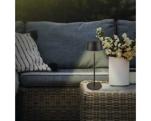 Lampe solaire décorative sur une table d''extérieur à côté d''un vase de fleurs et d''un canapé.