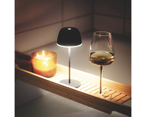 Scène avec une lampe de table sans fil, une bougie et un verre à vin sur une tablette de baignoire