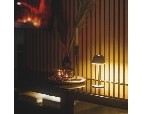 Scène de table décorative avec lampe, bougies et vase sur un buffet devant un mur en bois
