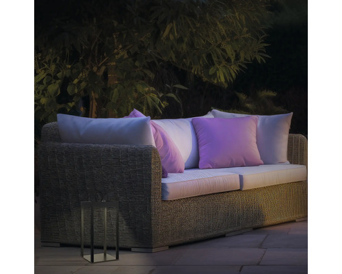 Scène de jardin avec canapé lounge en rotin, coussins et lanterne décorative d''extérieur
